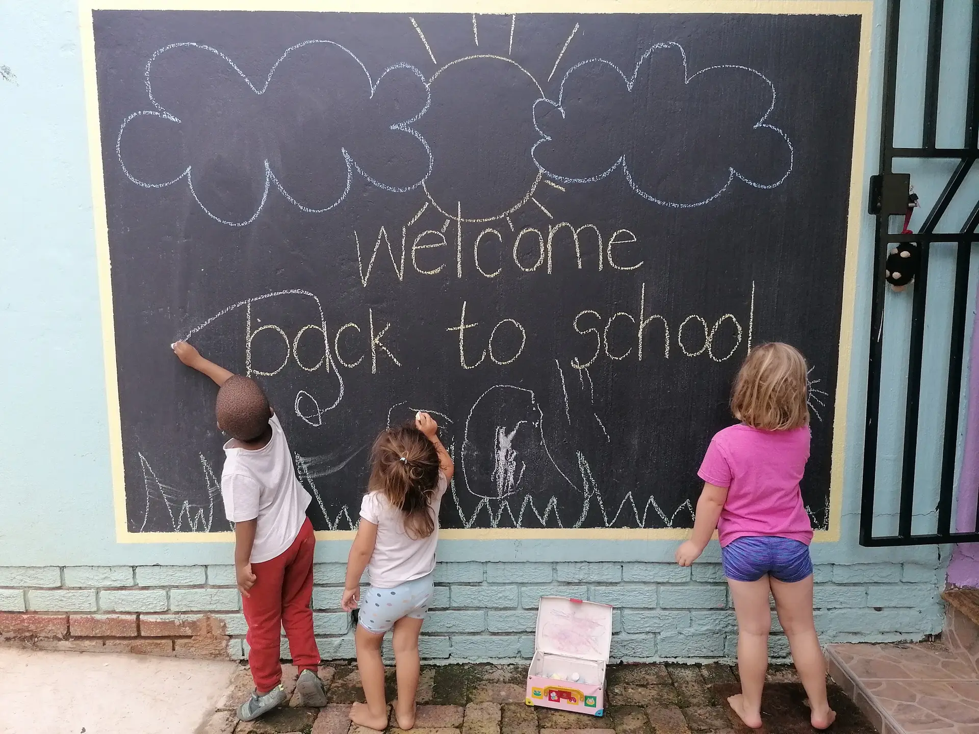 Children chalking under a 'Welcome back to school' board